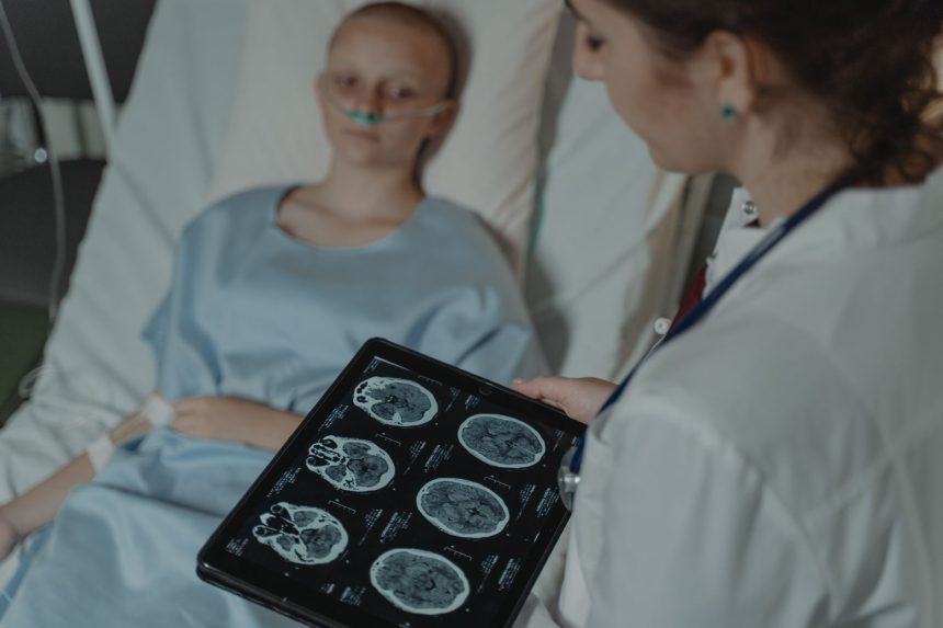 Profissional de saúde analisa imagens do cérebro em um tablet ao lado de um paciente internado.