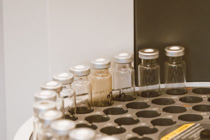Frascos de vidro organizados em um suporte dentro de um laboratório farmacêutico.