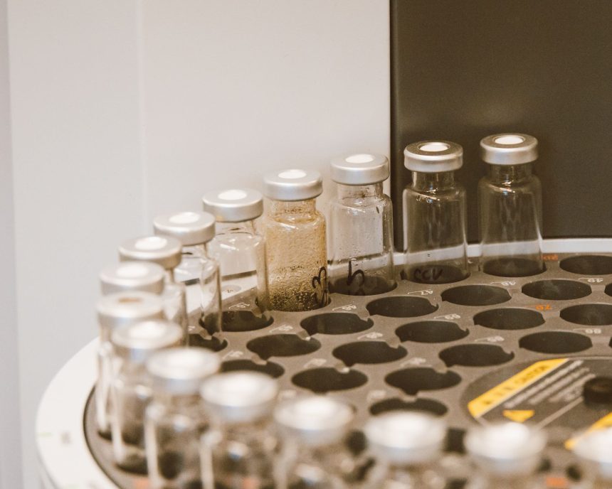 Frascos de vidro organizados em um suporte dentro de um laboratório farmacêutico.