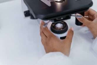 Cientista ajusta um microscópio em um laboratório para analisar uma amostra.