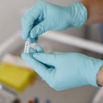 Mãos enluvadas seguram um frasco de vacina em um ambiente clínico