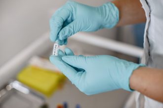 Mãos enluvadas seguram um frasco de vacina em um ambiente clínico