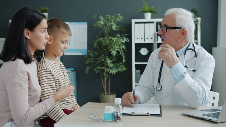 Médico conversa com uma mãe e uma criança durante uma consulta em uma clínica.