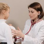 Médico examina uma criança com um estetoscópio durante um atendimento clínico.