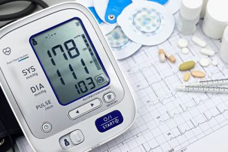 Monitor digital de pressão arterial, traçado de eletrocardiograma, comprimidos e instrumentos médicos sobre uma superfície clara.