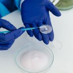 Pesquisadora com luvas manuseando uma placa de Petri em um laboratório com equipamentos científicos.
