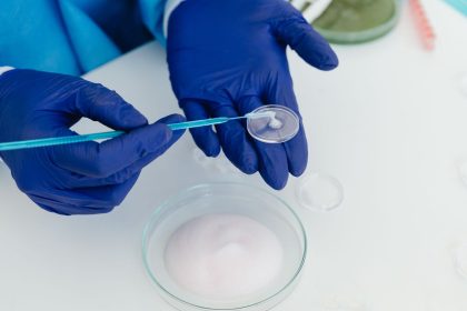 Pesquisadora com luvas manuseando uma placa de Petri em um laboratório com equipamentos científicos.
