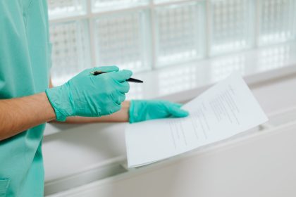 Profissional de saúde usando luvas segura e consulta um documento em ambiente clínico.