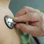 Médico ausculta o peito de uma criança com um estetoscópio em ambiente clínico.