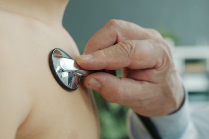 Médico ausculta o peito de uma criança com um estetoscópio em ambiente clínico.