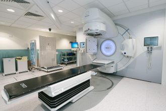 Acelerador linear de radioterapia em uma sala hospitalar preparada para tratamento oncológico.